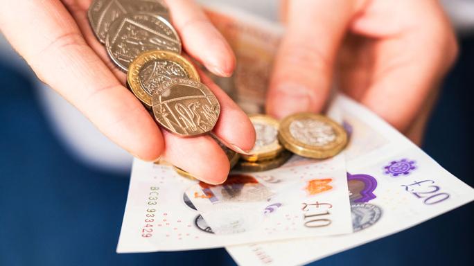 A hand holding UK cash