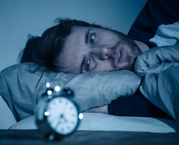 Man trying to sleep but looking at clock 
