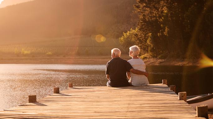 A retired couple sitting on the side of a lake