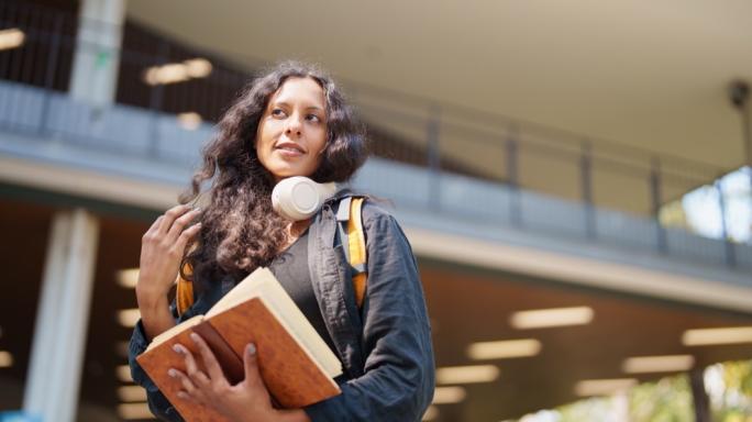 Young woman student carrying book and headphones