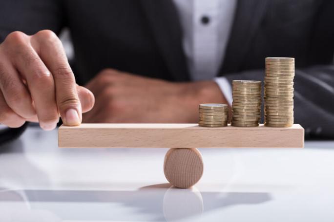 businessperson balancing stacked coins on wooden seesaw