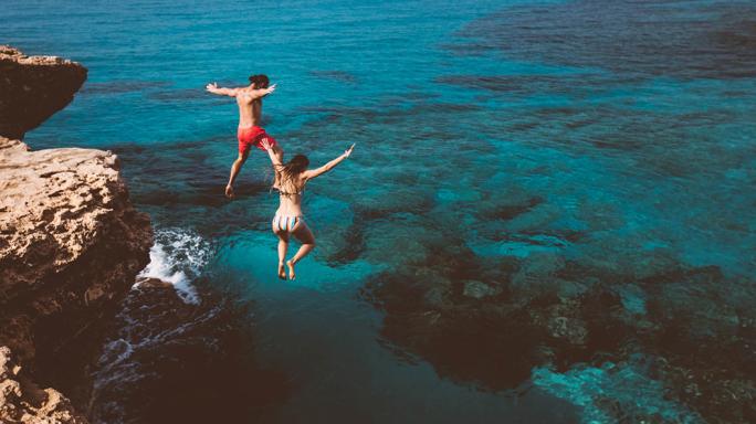 Couple, cliff jumping into ocean
