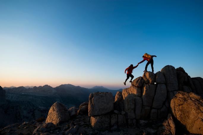 hiker helping another hiker step to the top of a hill