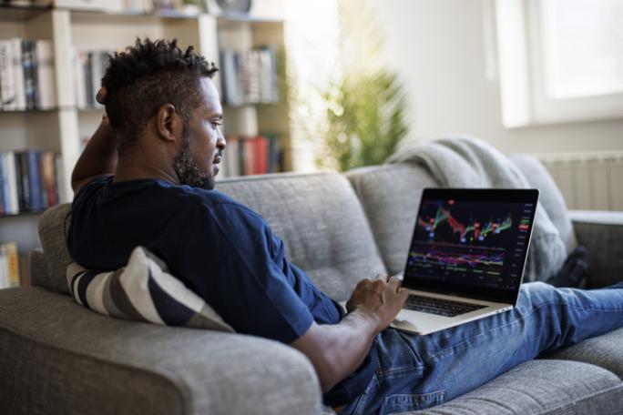 man sat on the sofa at home using laptop to analyse stock market