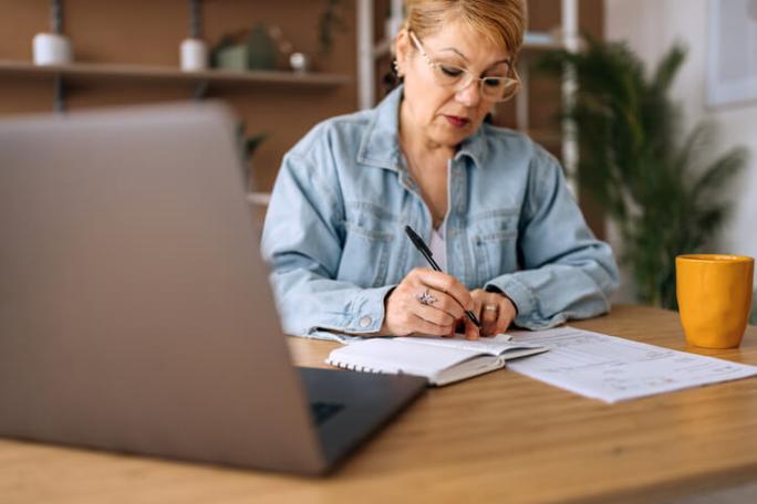 mature woman using laptop and taking notes