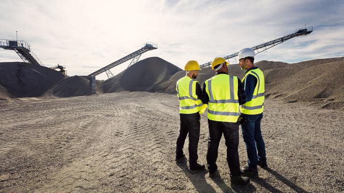 three mine workers talking with mining machinery in the background