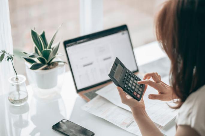 person using laptop and calculator by a window