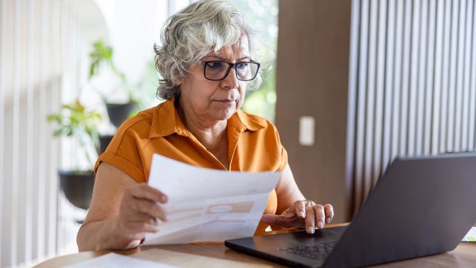 Woman using laptop, referring to paperwork