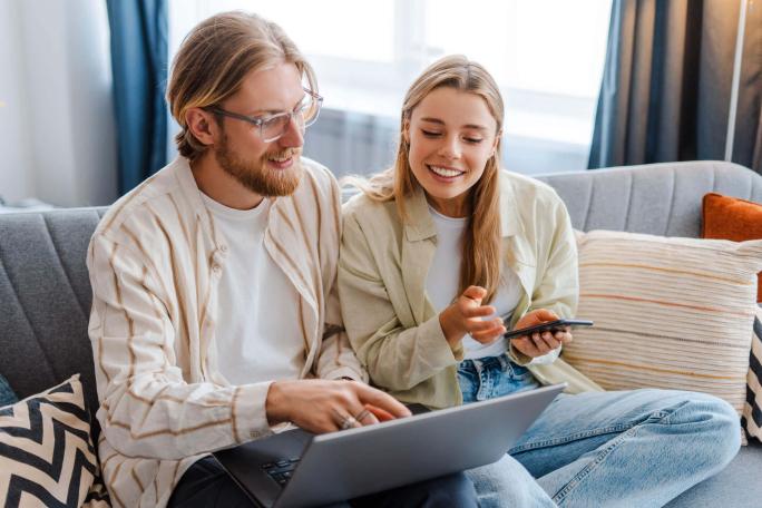 two people sat on sofa using laptop