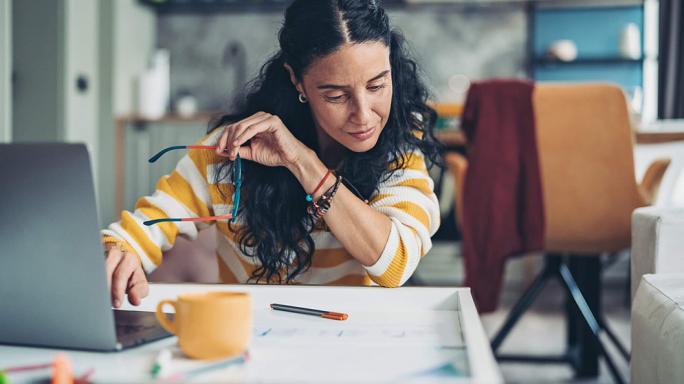 Woman holding her glasses using laptop