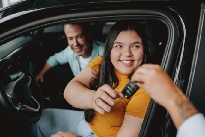 father and daughter sat inside a car with someone handing them car keys