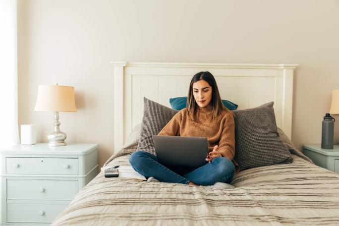 woman sitting on her bed using laptop and calculator
