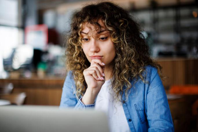 woman thinking while using laptop in a cafe