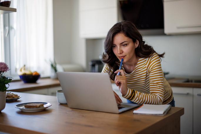 woman using laptop and resting a pen against her chin