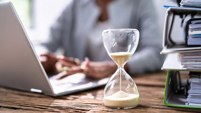 woman working on laptop with hourglass running next to her