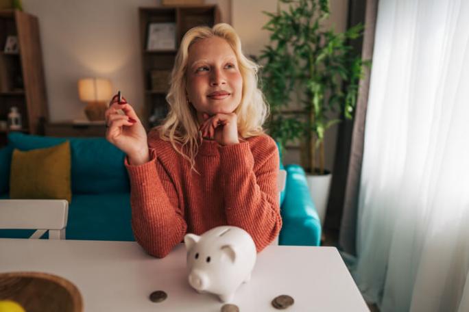 young woman saving money with piggy bank at home