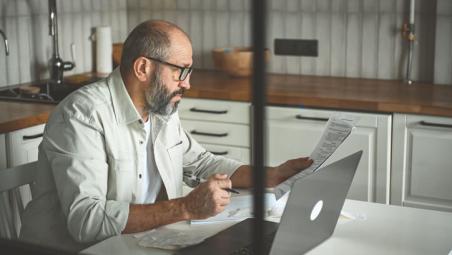 man-sat-in-front-of-a-laptop-with-papers-in-his-hands.jpg