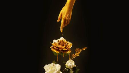 A finger dripping with gold touching a flower