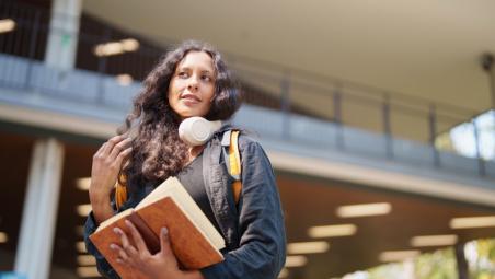 Young woman student carrying book and headphones