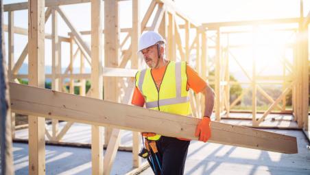 builder carrying a wooden beam on building site
