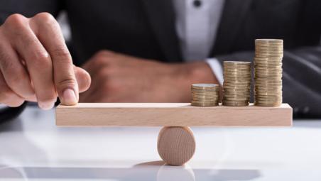 businessperson balancing stacked coins on wooden seesaw