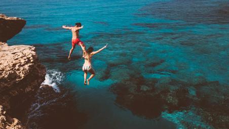 Couple, cliff jumping into ocean