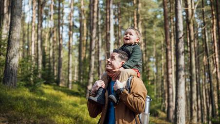 father carrying child on his shoulders in the forest