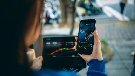 person looking at graphs on phone screen and laptop screen