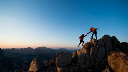 hiker helping another hiker step to the top of a hill