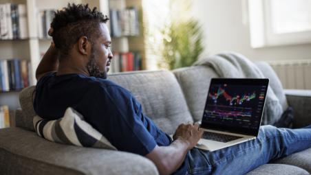 man sat on the sofa at home using laptop to analyse stock market