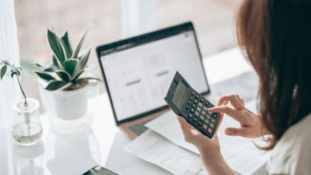 person using laptop and calculator by a window