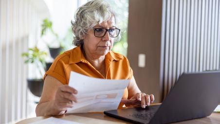 Woman using laptop, referring to paperwork