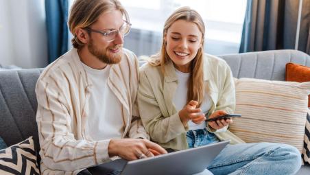 two people sat on sofa using laptop