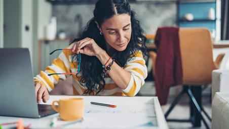 Woman holding her glasses using laptop