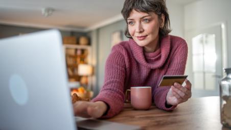 woman sat at desk at home using laptop and holding credit card