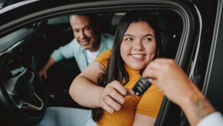 father and daughter sat inside a car with someone handing them car keys