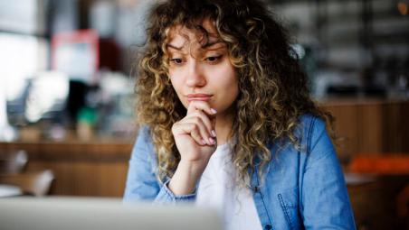 woman thinking while using laptop in a cafe