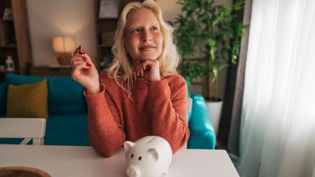 young woman saving money with piggy bank at home